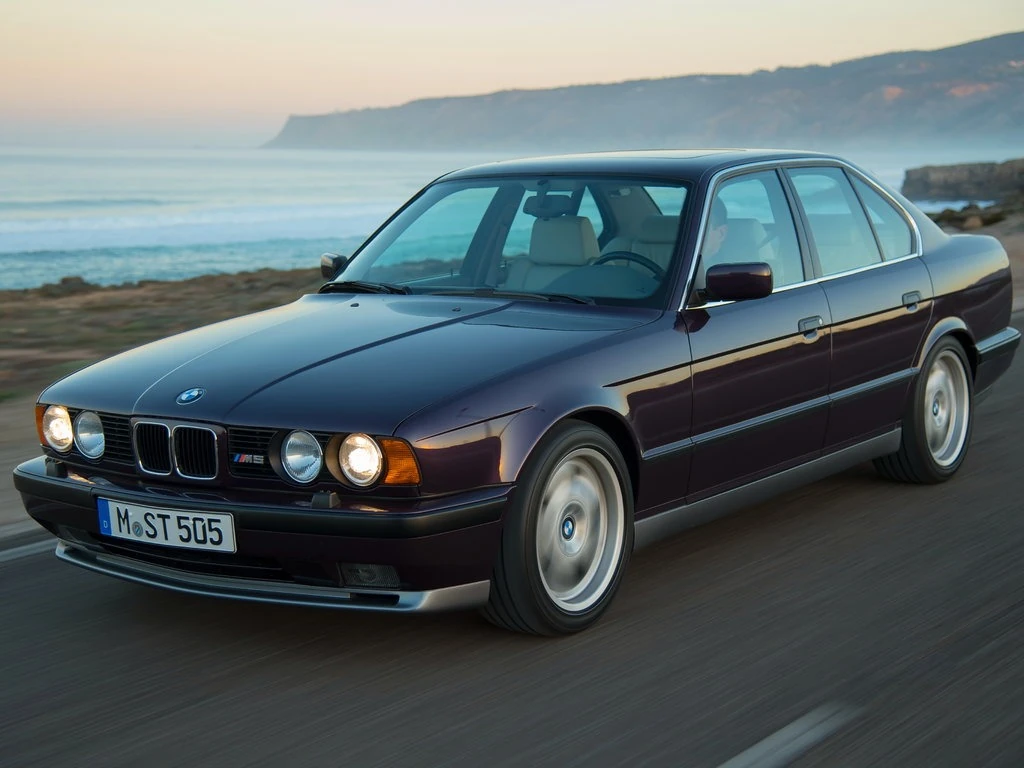 Чорний BMW седан 90-х років на узбережжі з морем і скелями позаду